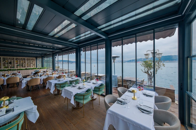 Commercial waterfront dining space enclosed by integrated glass and a bioclimatic pergola.