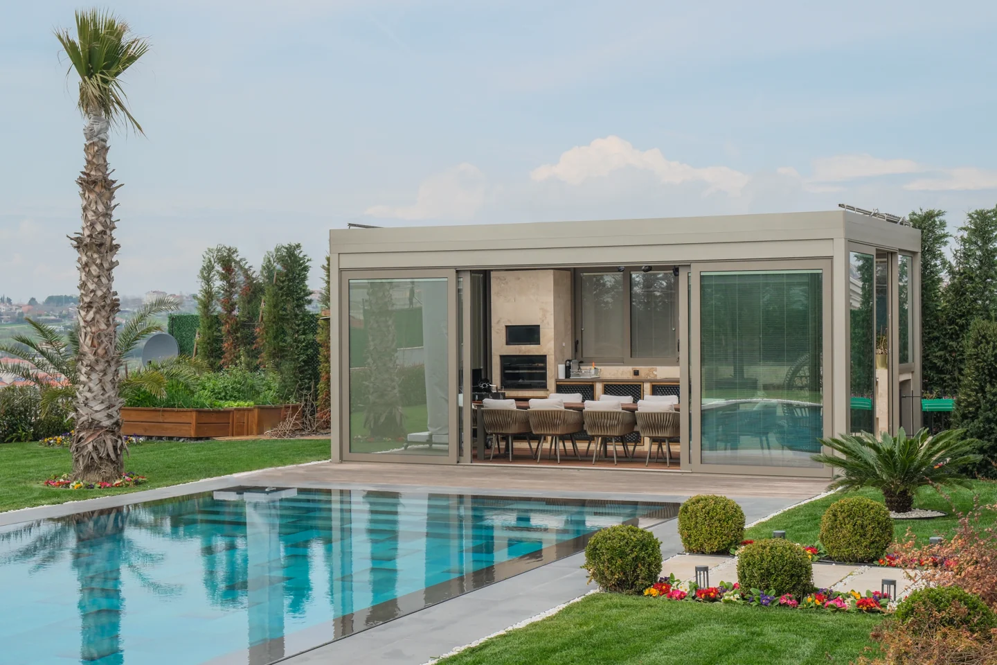 Glass-enclosed residential pergola beside a landscaped swimming pool.